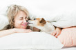 Blonde beautiful Woman and dog playfully indulge in fun on the bed. Dog bites the girl's nose. Happy time with pets