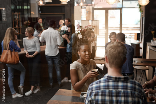 Fotografía African woman talking with friend inside busy coffee shop