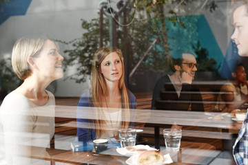 Wall Mural - Woman listening as friends talk at a busy modern cafe