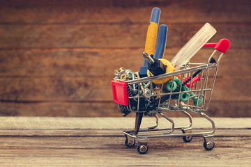 Shopping cart with construction tools on the old wood background. Toned image. 