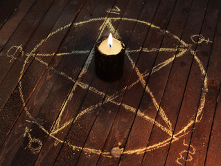 black candle in pentagram on wooden planks