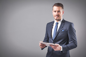 Handsome businessman holding a digital tablet on grey background