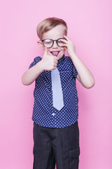 Wall Mural - Little adorable boy in tie and glasses. School. Fashion. Studio portrait over pink background