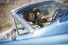 A Young Couple, Man And Woman In A Pale Blue Convertible On The Open Road 
