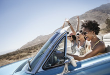Three Young People In A Pale Blue Convertible Car, Driving On The Open Road Across A Flat Dry Plain, 