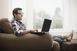 © Mint Images - A man seated on a sofa, using  a laptop computer,