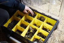 A Man Working In A Cycle Shop, Reaching For Parts In A Box Of Spares, 