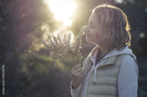 Fotomural Girl smelling the fragrance of a rosemary twig at sunset in the middle of the forest