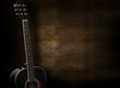 Black acoustic guitar on dark yellow wooden background.
