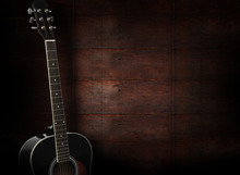 Black Acoustic Guitar On Dark Red Wooden Background.