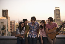 A Small Group Of Friends Gathered On A Rooftop Terrace Overlooking A City At Twilight, 
