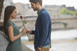 © Mint Images - A couple in a romantic setting by a river, A man offering a woman a red rose,