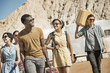 © Mint Images - A group of people walking in a line in open desert country, carrying their cases, on a road trip,