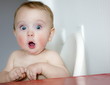 Leinwandbild Motiv surprised kid sitting at table. child's eyes widened and mouth opened in amazement. copy space for your text