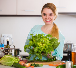 Wall Mural - Young woman chopping lettuce and herbs in kitchen