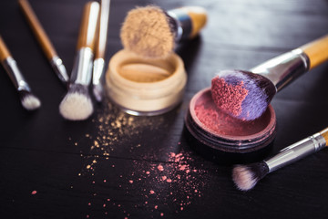 make up brushes with powder and rouge on a black wooden backgrou