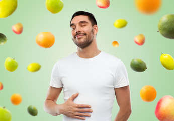 happy full man touching tummy over falling fruits