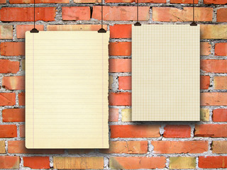 Close-up of two hanged blank brown paper sheet frames with clips against orange brick wall background