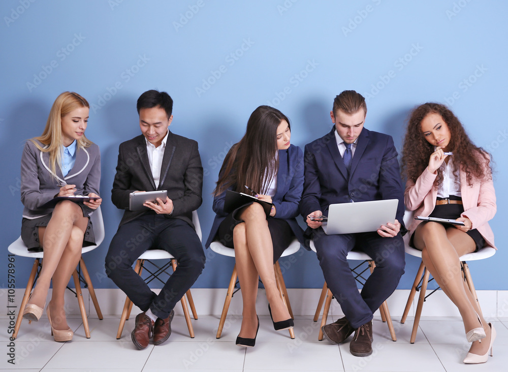 Young people sitting on a chairs, making notes and using devices in blue hall