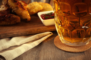 Canvas Print - Glass of beer and chicken wings on wooden table, close up