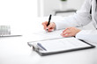 © rogerphoto - Close-up of a female doctor filling  out application form , sitting at the table in the hospital
