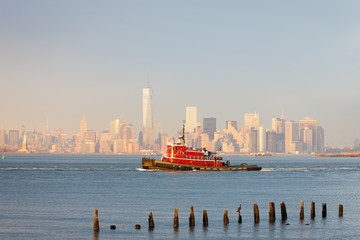 Wall Mural - Tugboat in New York Harbor in afternoon soft winter light with the Financial District of Lower Manhattan in background. New York City