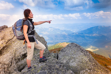 Young happy woman with backpack standing on top of the mountain.