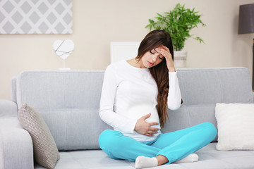 Wall Mural - Pregnant woman with headache sitting on sofa in the room