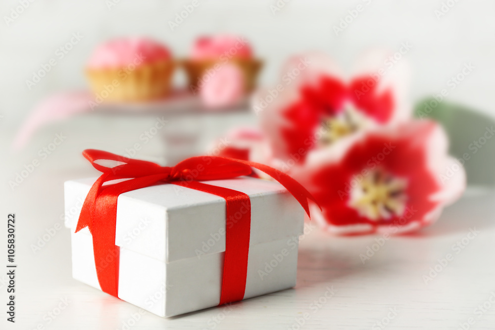 Present box, fresh tulips and delicious cupcakes on wooden table closeup