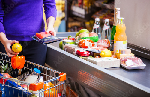 Fotografía Young woman putting goods on counter in supermarket