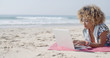 © Dash - Young girl working on laptop while lying on a beach blanket