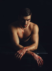 beautiful pumped man with a naked torso and a tattoo , hands in the blood , halloween, posing on a b