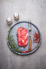 Raw Ribeye Steak with spices and meat fork on gray stone plate , top view