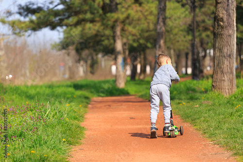 Fotografia, Obraz Little boy riding his scooter at the park