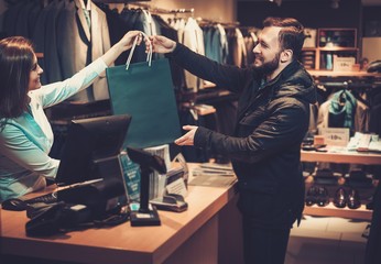 Wall Mural - Happy handsome man taking shopping bag from saleswoman in a suit shop.