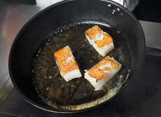 Pan fried golden fish fillet cubes, frying in real butter, in a non stick rustic pan.