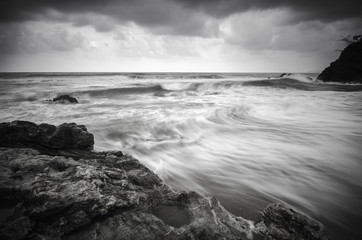 Wall Mural - black and white image wave flow on the sandy and rocky beach with dark and dramatic cloud.