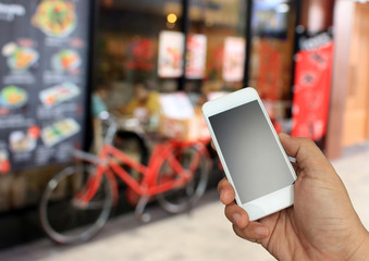 Wall Mural - hand holding the smartphone on blurred restaurent background