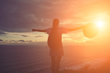 Wall Mural - Silhouette of young girl with hat looking far away at sunset on a beach (intentional sun glare and vintage color)