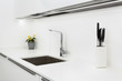 Modern designer chrome water tap over stainless steel kitchen sink. Interior of bright white kitchen