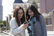 © Monet - Two women are laughing while looking at the smartphone outside