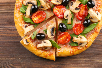 Sliced delicious tasty pizza with vegetables on wooden table