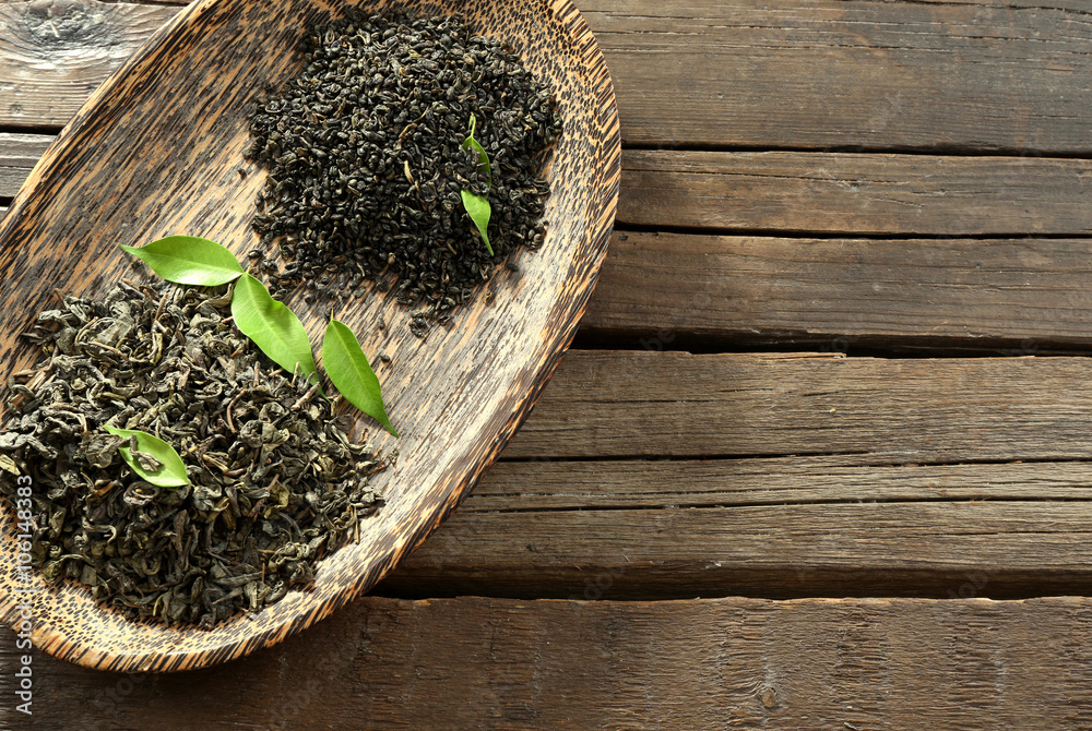Dry tea in plate with green leaves on wooden table background