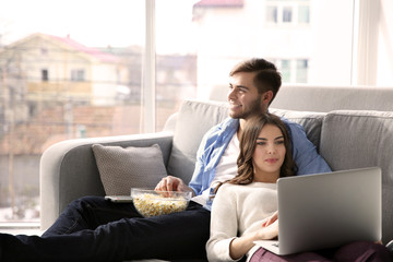 Wall Mural - Young man watching TV and woman using laptop on a sofa at home