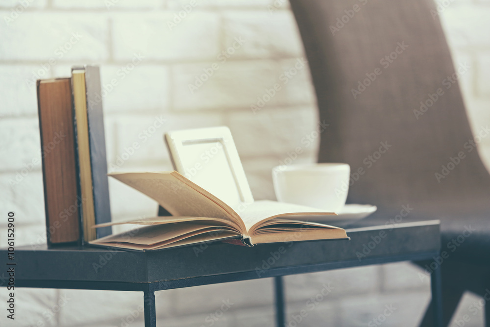 Open book with cup on black small table against white brick wall, close up