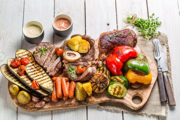 Grilled vegetables and steak with herbs on white table