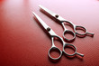 Professional metal scissors lying on red leather surface, close up