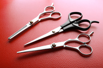 Poster - Professional scissors with black and metal handles lying on red leather surface, close up