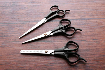 Canvas Print - Three professional metal scissors with black handles lying on the wooden table, close up