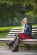 © sergeyzapotylok - Closeup outdoors portrait of young adorable blonde woman sitting on the park bench  in windy weather conditions with green blurry background